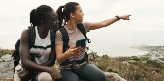 Two hikers checking their phone on a coastal trail